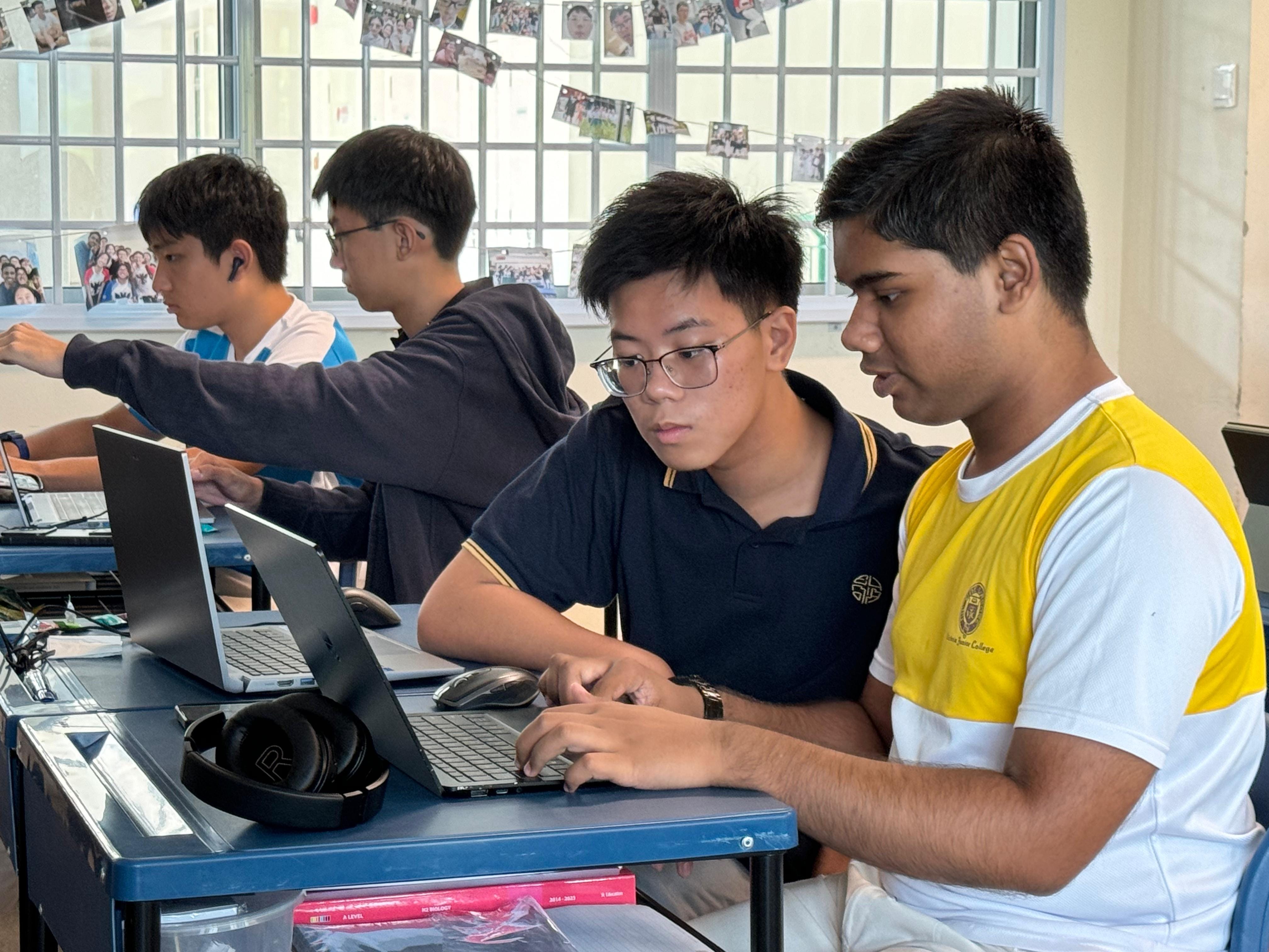 Students collaborating on laptops in a classroom setting, focused on tasks.
